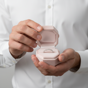 Person holding a pink jewelry box with a ring inside, wearing a white shirt.