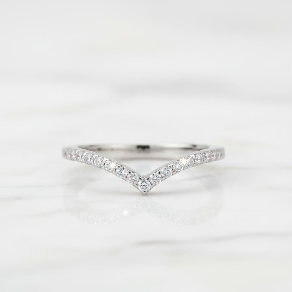 A delicate silver V-shaped ring set with small clear pavé stones, resting on a white marble surface.