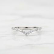 A delicate silver V-shaped ring set with small clear pavé stones, resting on a white marble surface.