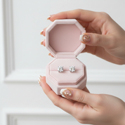 Pink hexagonal jewelry box with diamond earrings held by a hand on a light background