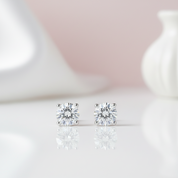 Diamond stud earrings on a reflective surface with a soft pink background