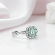 Ring with a green gemstone and diamond halo on a light background