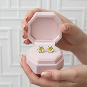 Pink jewelry box with yellow gemstone earrings held by a hand against a white background