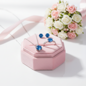Jewelry set with blue gemstones in a pink jewelry box, accompanied by flowers.