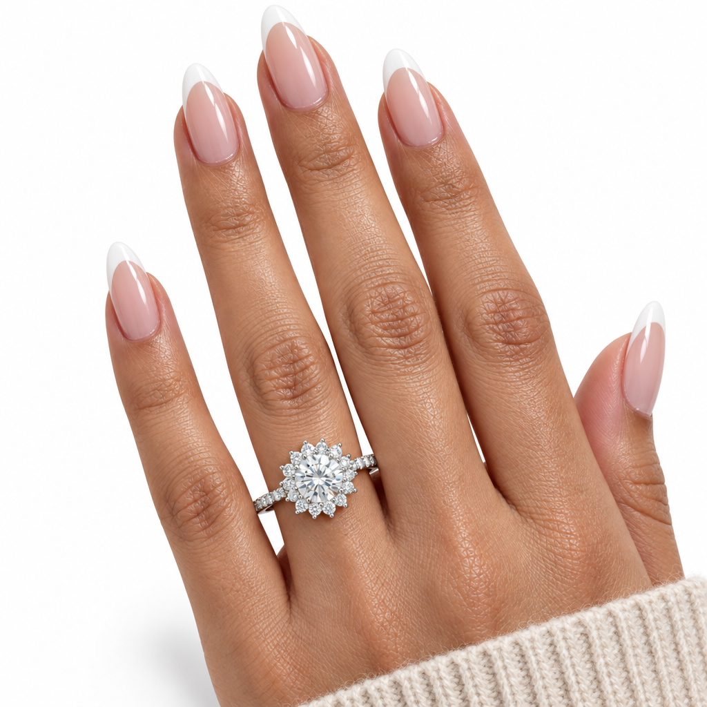A close-up of a hand with long, manicured French-tip nails wearing a silver-toned diamond ring with a round cluster center stone and smaller side stones, set against a clean white background.