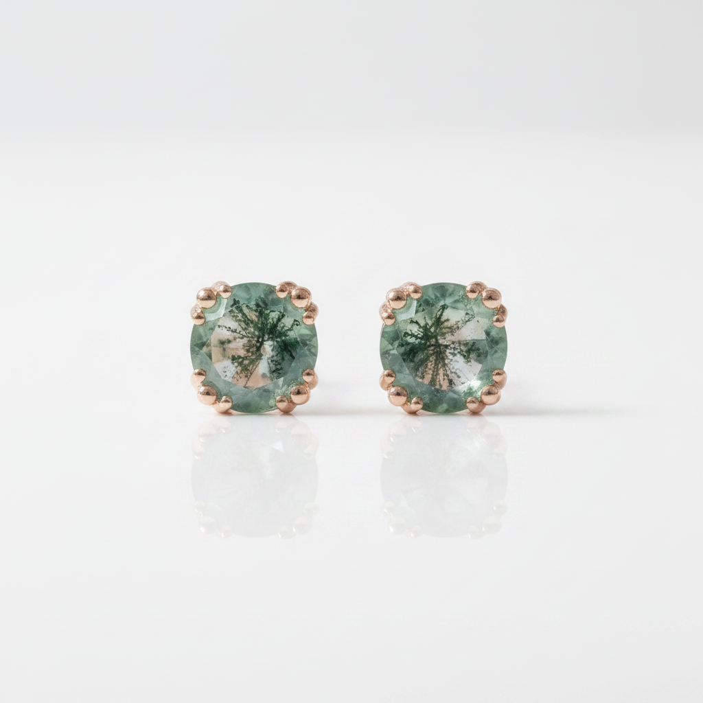 A pair of oval-cut green gemstone stud earrings set in rose gold with a beaded border, displayed on a clean white reflective surface.