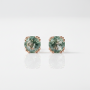 A pair of oval-cut green gemstone stud earrings set in rose gold with a beaded border, displayed on a clean white reflective surface.
