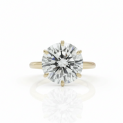 A classic solitaire engagement ring featuring a round brilliant-cut diamond set in a yellow gold four-prong band, shown on a clean white background with a soft reflection below.