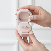 Hand holding a pink jewelry box with a ring inside against a white background