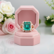 Emerald green ring in a pink box with flowers in the background