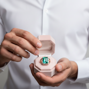 Person holding a ring with a green gemstone in a white box.
