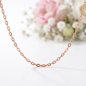 A delicate rose gold chain necklace with a polished finish, displayed in a curved shape against a clean white background with a subtle reflection.