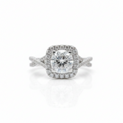 A silver-toned halo ring featuring a cushion-cut center diamond surrounded by a double halo of small round diamonds, set on a split shank band, photographed on a clean white background with a soft reflection below.
