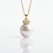 A gold pendant necklace featuring a large, lustrous white pearl pendant under a small crown setting with tiny clear stones, suspended from a gold chain on a clean white background.