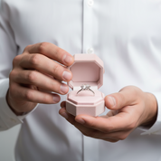 Person holding a pink jewelry box with a ring inside against a white background