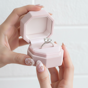 Hand holding a pink jewelry box with a ring inside on a light background