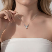 A close-up lifestyle shot of a model wearing a delicate silver angel wing pendant necklace with a small pearl drop, styled with a white strapless top.