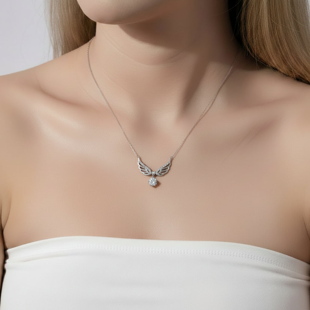 A close-up of a woman wearing a delicate silver wing pendant necklace with a small clear gemstone, paired with a white strapless top.