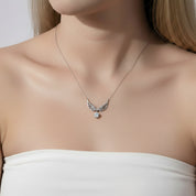 A close-up of a woman wearing a delicate silver wing pendant necklace with a small clear gemstone, paired with a white strapless top.