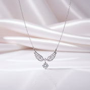 A silver angel wing pendant necklace with a sparkling clear gemstone, displayed on a soft, draped white satin fabric background.