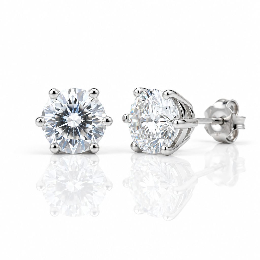 A pair of round-cut diamond stud earrings in a six-prong setting with polished silver-toned metal, shown on a clean white background with soft reflections below.