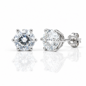 A pair of round-cut diamond stud earrings in a six-prong setting with polished silver-toned metal, shown on a clean white background with soft reflections below.