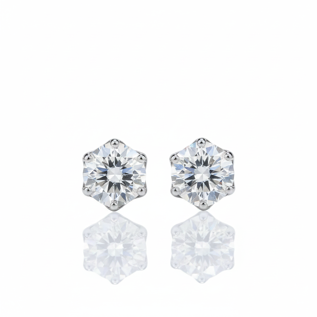A pair of round-cut stud earrings with clear faceted gemstones in a silver-toned setting, shown on a white background with soft reflections below.