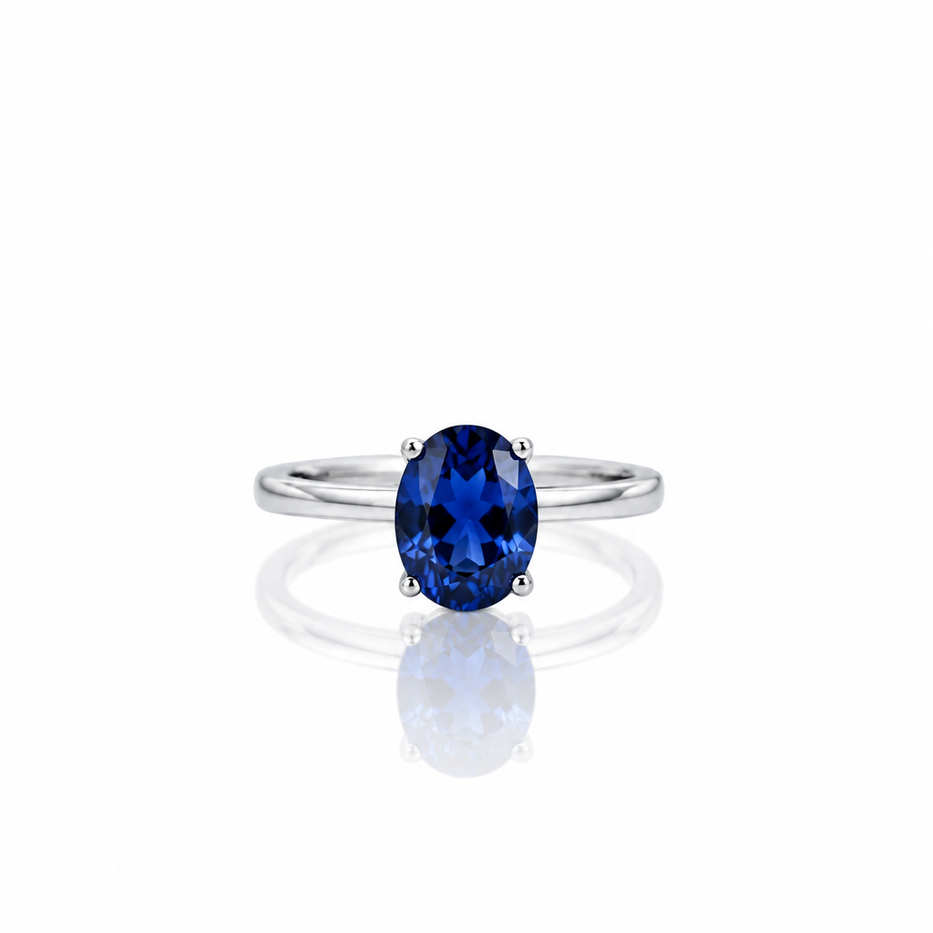 An oval-cut deep blue gemstone ring set in a polished silver band, centered on a clean white background with a soft reflection below.
