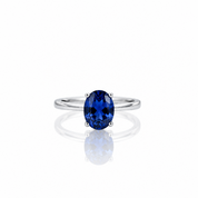 An oval-cut deep blue gemstone ring set in a polished silver band, centered on a clean white background with a soft reflection below.