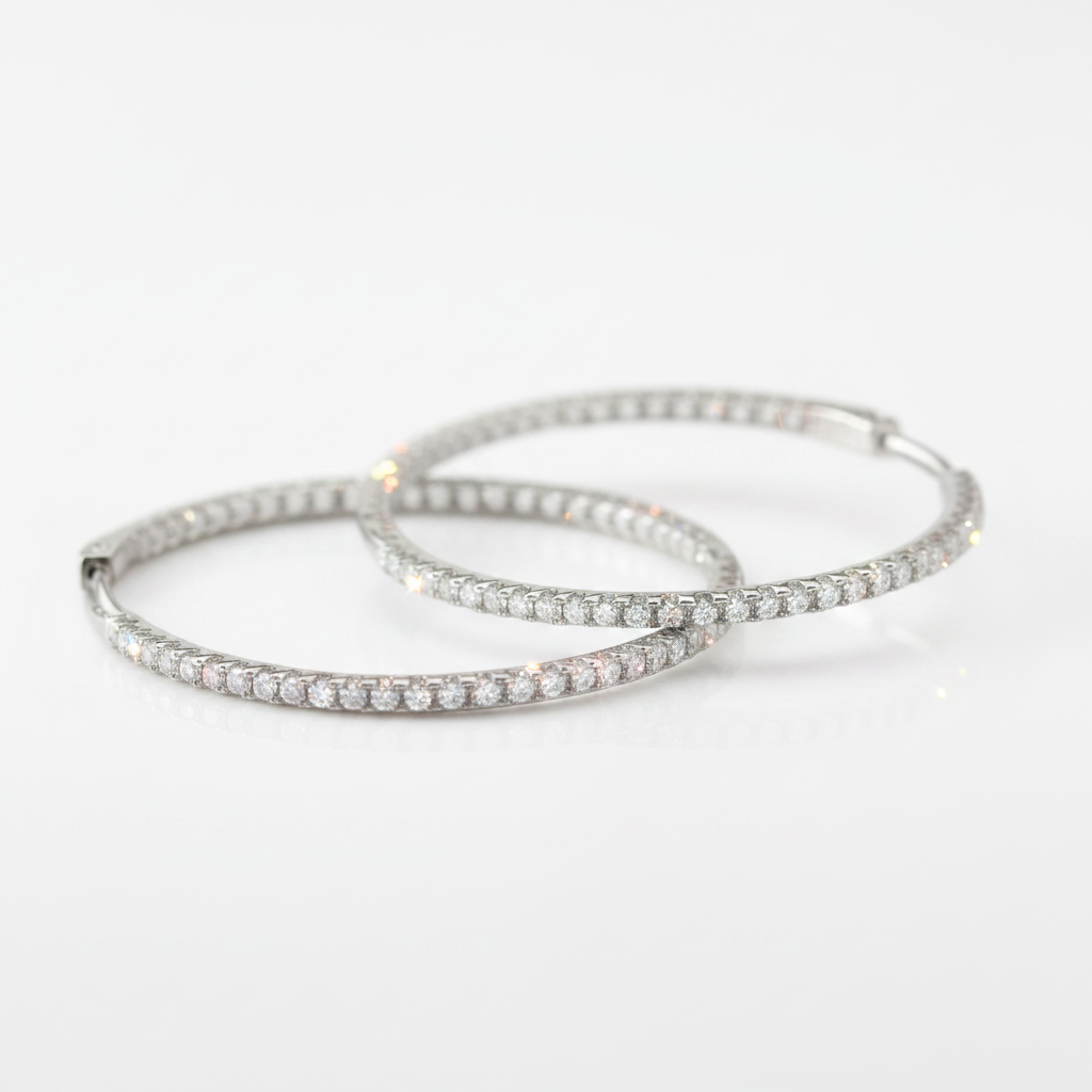 A pair of silver hoop earrings paved with small clear stones, photographed on a clean white background.