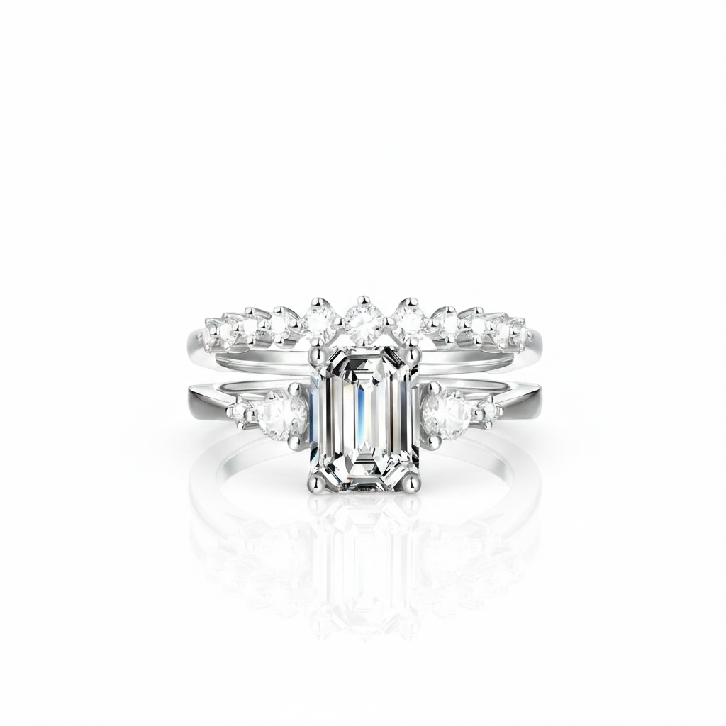 A white gold or platinum engagement ring set with a rectangular emerald-cut center stone and smaller accent stones along the shoulders, shown on a clean white background with a soft reflection below.