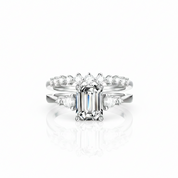 A white gold or platinum engagement ring set with a rectangular emerald-cut center stone and smaller accent stones along the shoulders, shown on a clean white background with a soft reflection below.