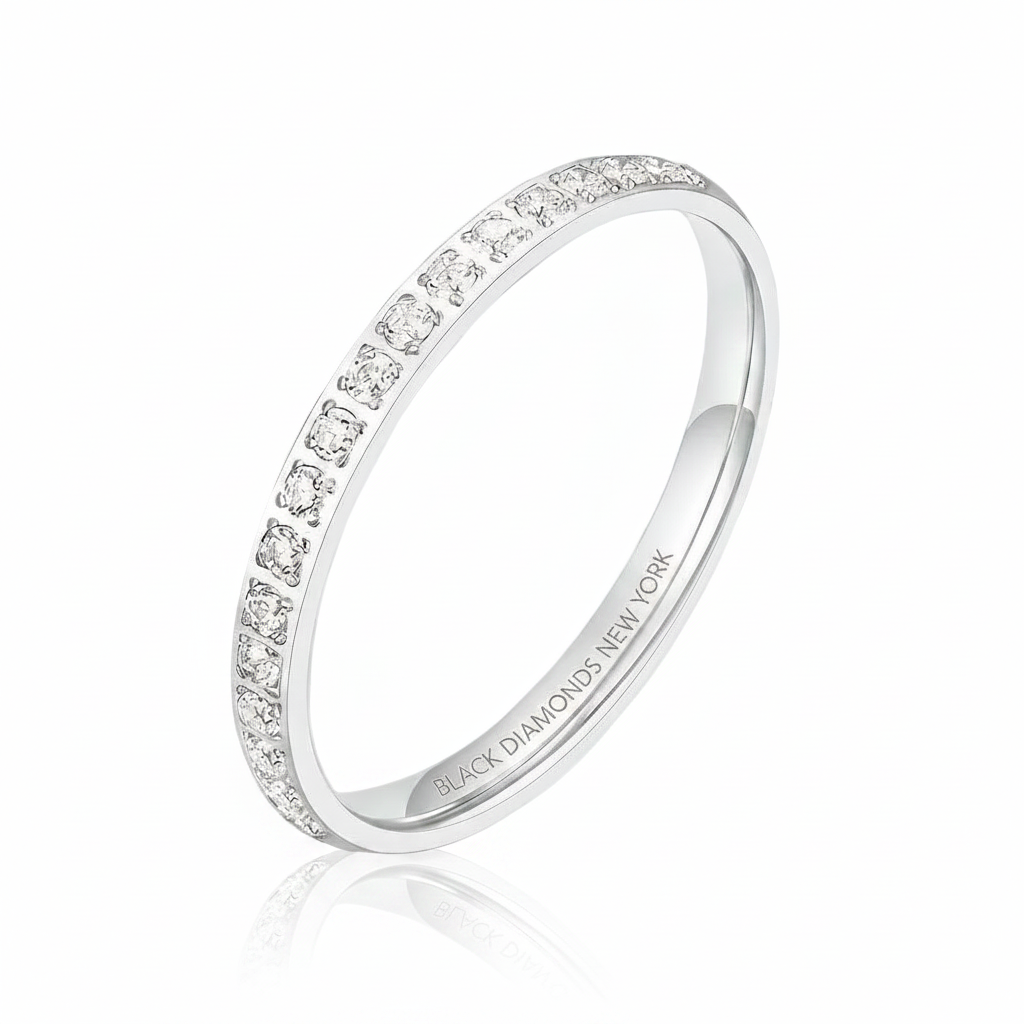 A silver eternity ring featuring a single row of round-cut clear gemstones, shown on a clean white background with a soft reflection. The inside of the band is engraved with 'BLACK DIAMONDS NEW YORK'.