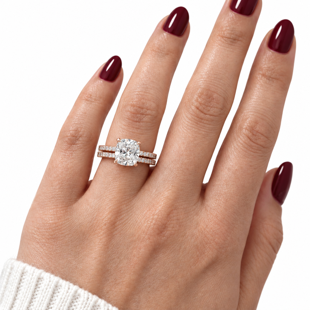 A close-up of a hand with dark burgundy nail polish wearing a diamond engagement ring with a matching pavé band, set against a clean white background.