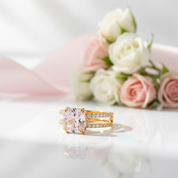 Gold ring with a pink gemstone on a white surface with flowers in the background