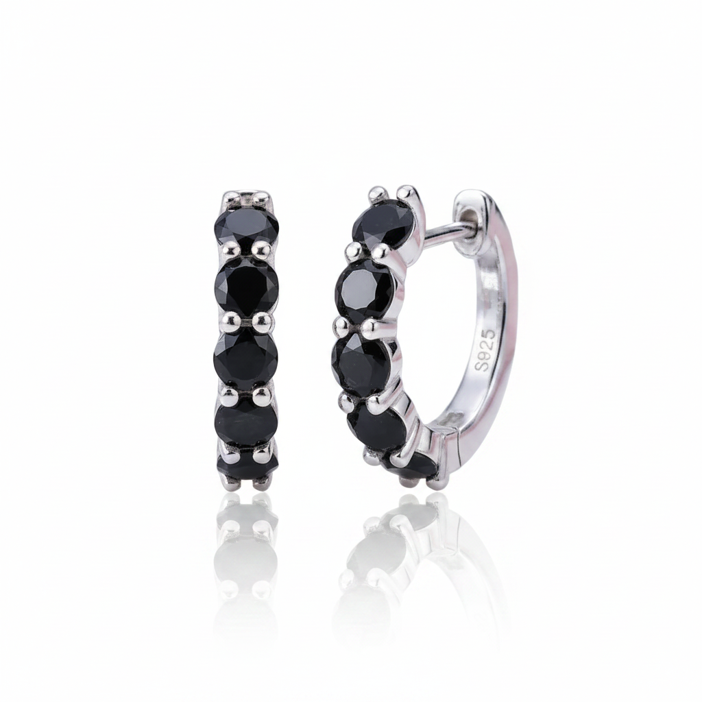 A pair of small silver huggie hoop earrings with a row of round black gemstones, shown on a clean white background with a soft reflection below.