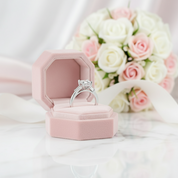 Silver ring in a pink box with a bouquet of flowers in the background