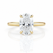 An oval diamond engagement ring with a yellow gold band, featuring a brilliant-cut center stone in a four-prong setting on a clean white background with a soft reflection below.