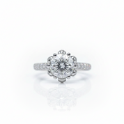 A silver-tone halo engagement ring featuring a round-cut center stone and pavé-set side stones, centered on a clean white background with a soft reflection below.