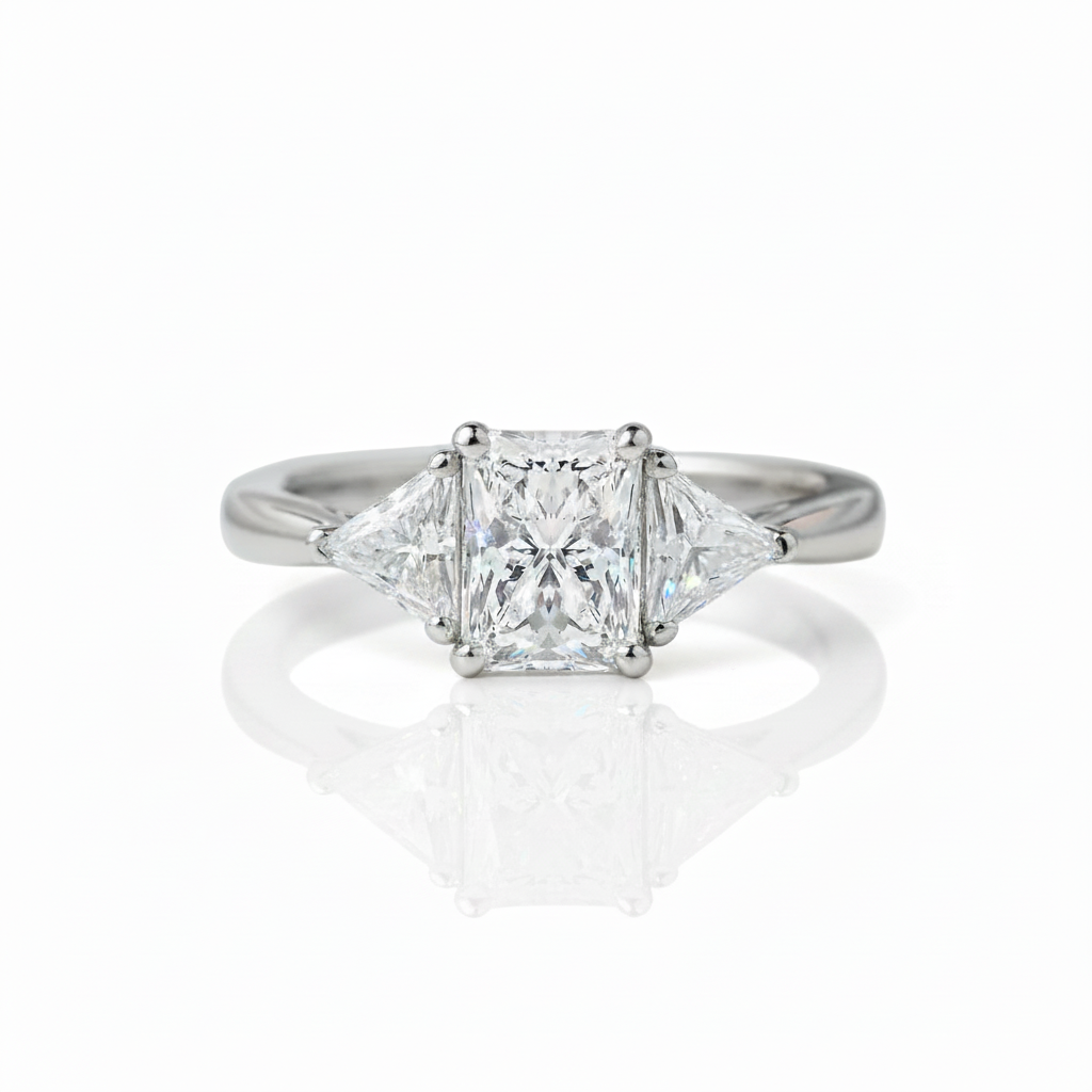 A classic three-stone diamond ring featuring a princess-cut center stone flanked by two smaller round diamonds, set in a polished silver-colored band on a reflective white surface.