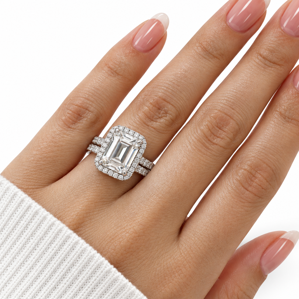 A close-up of a hand wearing a silver-toned emerald-cut halo ring with pavé accents, set against a clean white background.