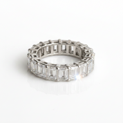 A silver eternity ring featuring baguette-cut clear gemstones, photographed on a clean white reflective surface.