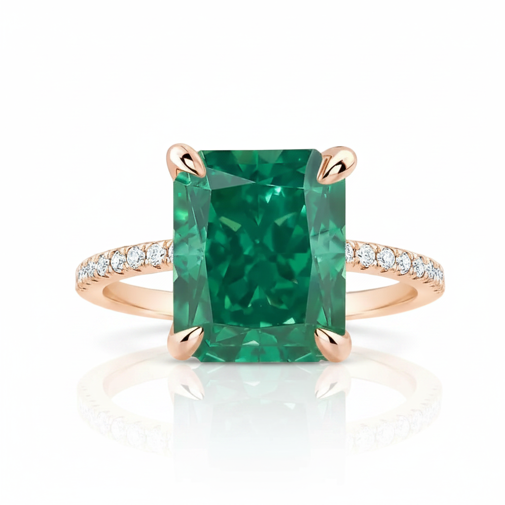 An emerald-cut green gemstone ring with a rose gold band accented by small pavé diamonds, shown on a clean white background with a soft reflection.