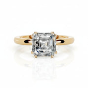 An emerald-cut diamond solitaire ring set in a yellow gold band, shown on a clean white background with a soft reflection below.