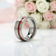 Silver ring with red inlay on a white surface with flowers in the background