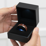 Hand holding a black jewelry box with a wooden ring inside on a white background