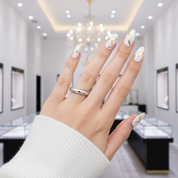 Hand with white nail polish and a ring, blurred jewelry store interior in the background