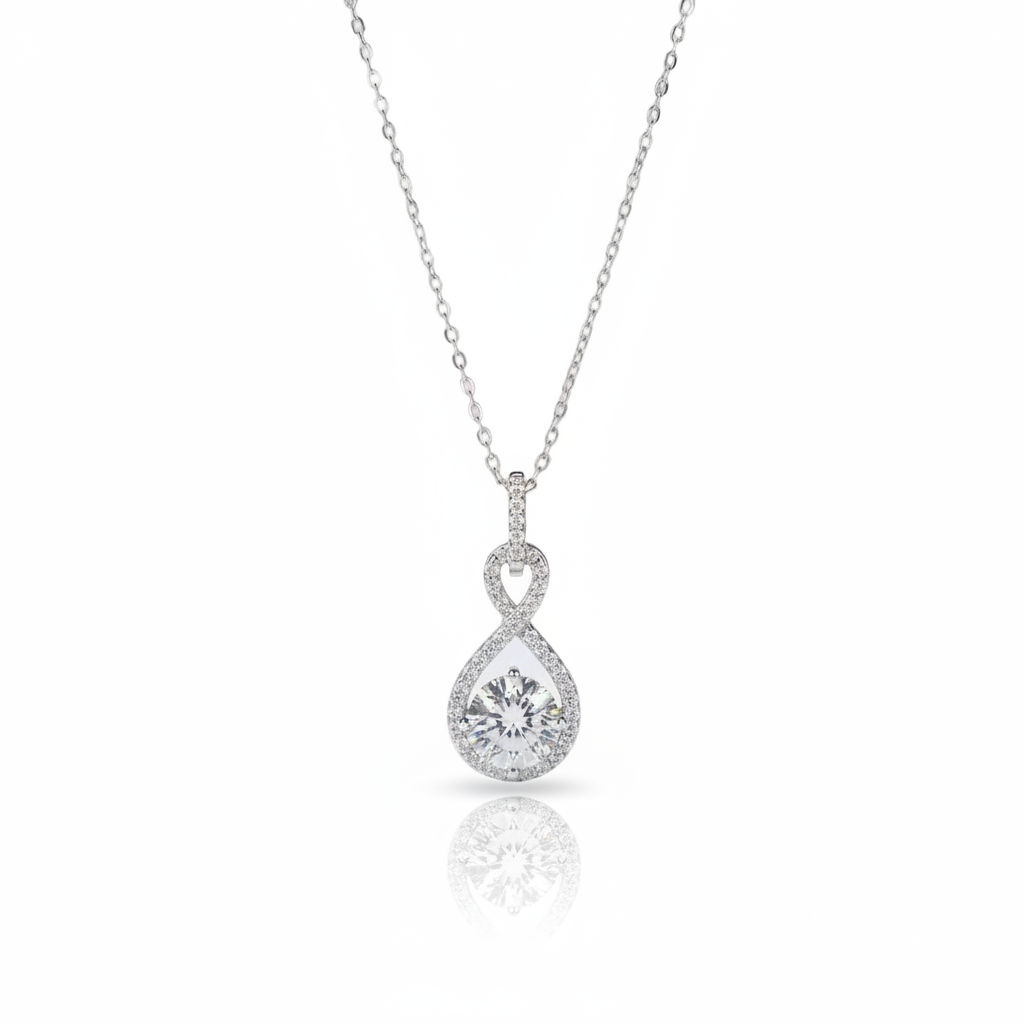 A silver pendant necklace featuring a teardrop-shaped pear-cut center stone surrounded by a halo of small round stones, suspended from a delicate silver chain on a white background with a soft reflection below.