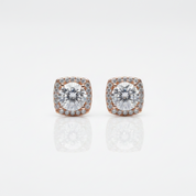A pair of square cushion-cut halo stud earrings featuring a central clear gemstone surrounded by a halo of smaller clear stones in rose gold, set against a clean white background with a soft reflection below.