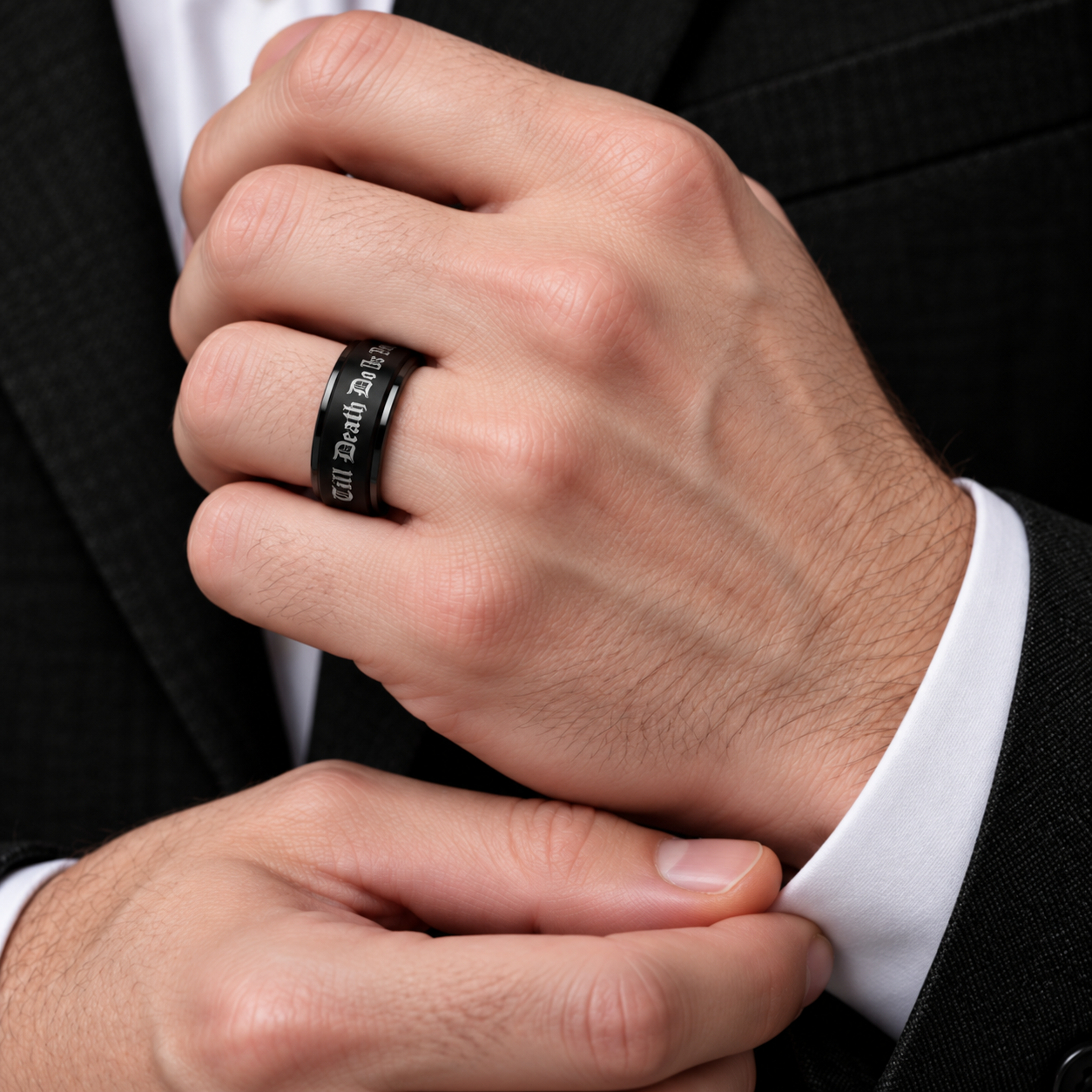 A close-up of a man's hands adjusting his dress shirt cuff while wearing a black engraved ring on his finger. He is dressed in a black suit jacket.